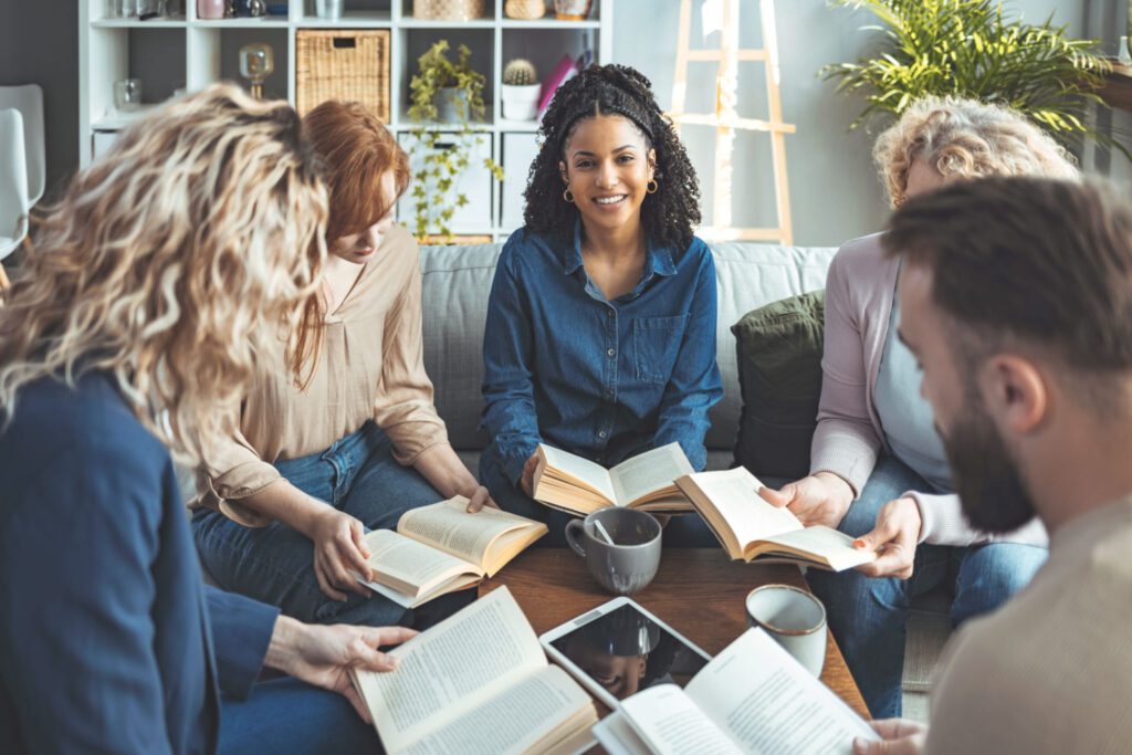 Group of diverse young adults reading books together in a cozy room.