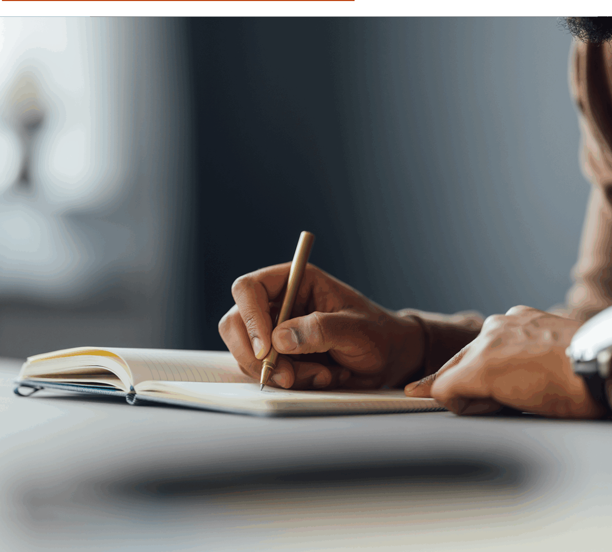 Person writing in a notebook with a pencil indoors.