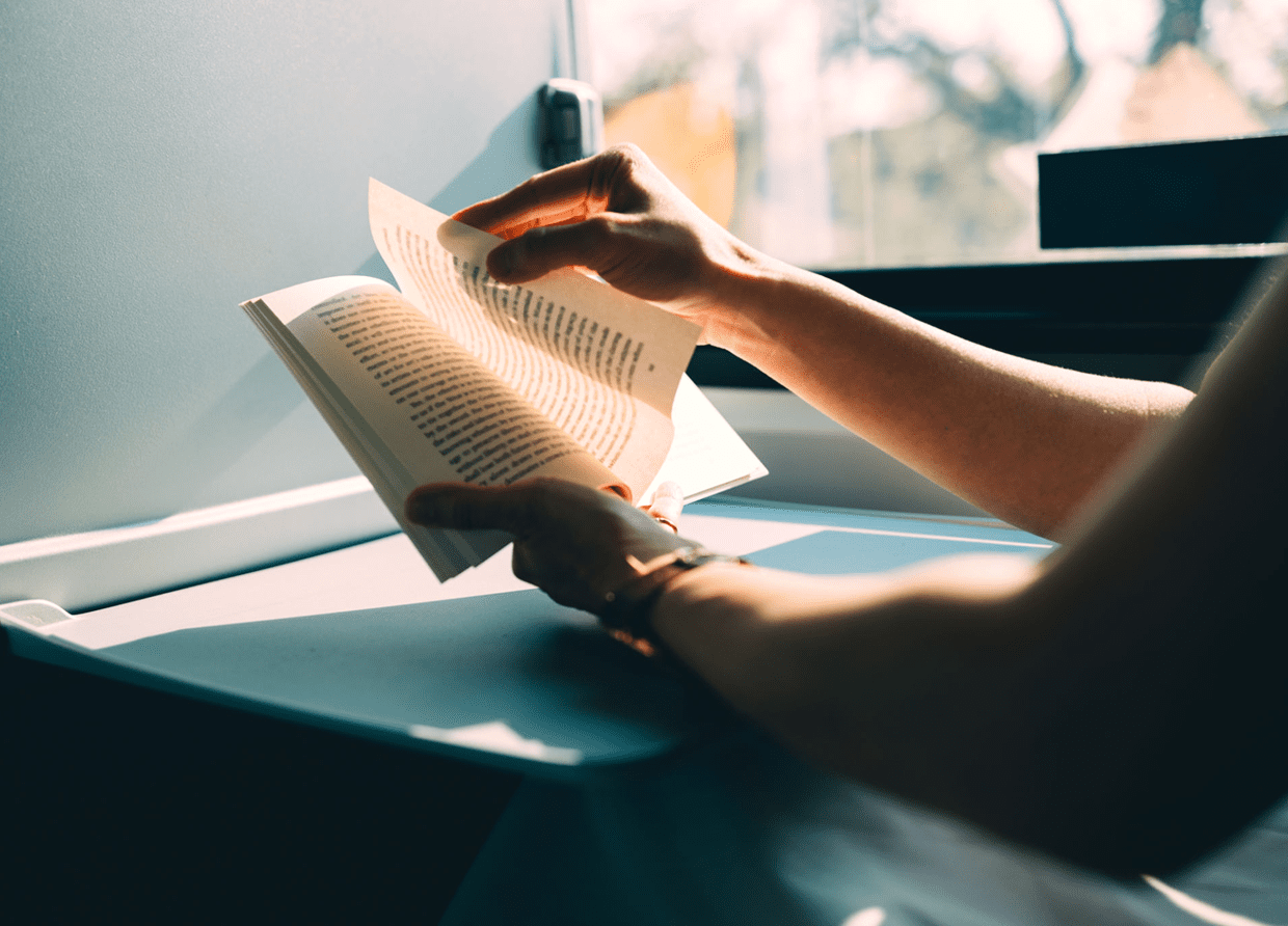 Person reading a book by a sunny window.