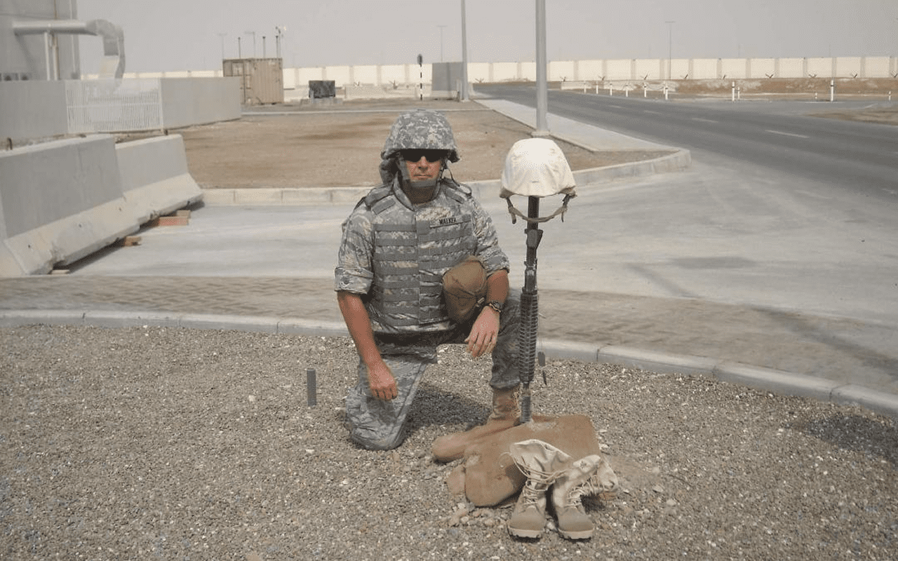 A soldier kneeling beside a dog in a desert environment.