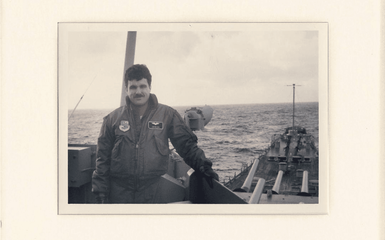 Man standing on a boat deck in cold weather, holding a dog.