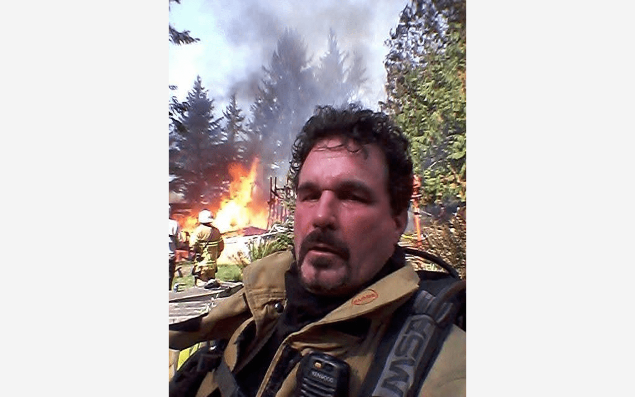 Firefighter with smoky fire scene in background.